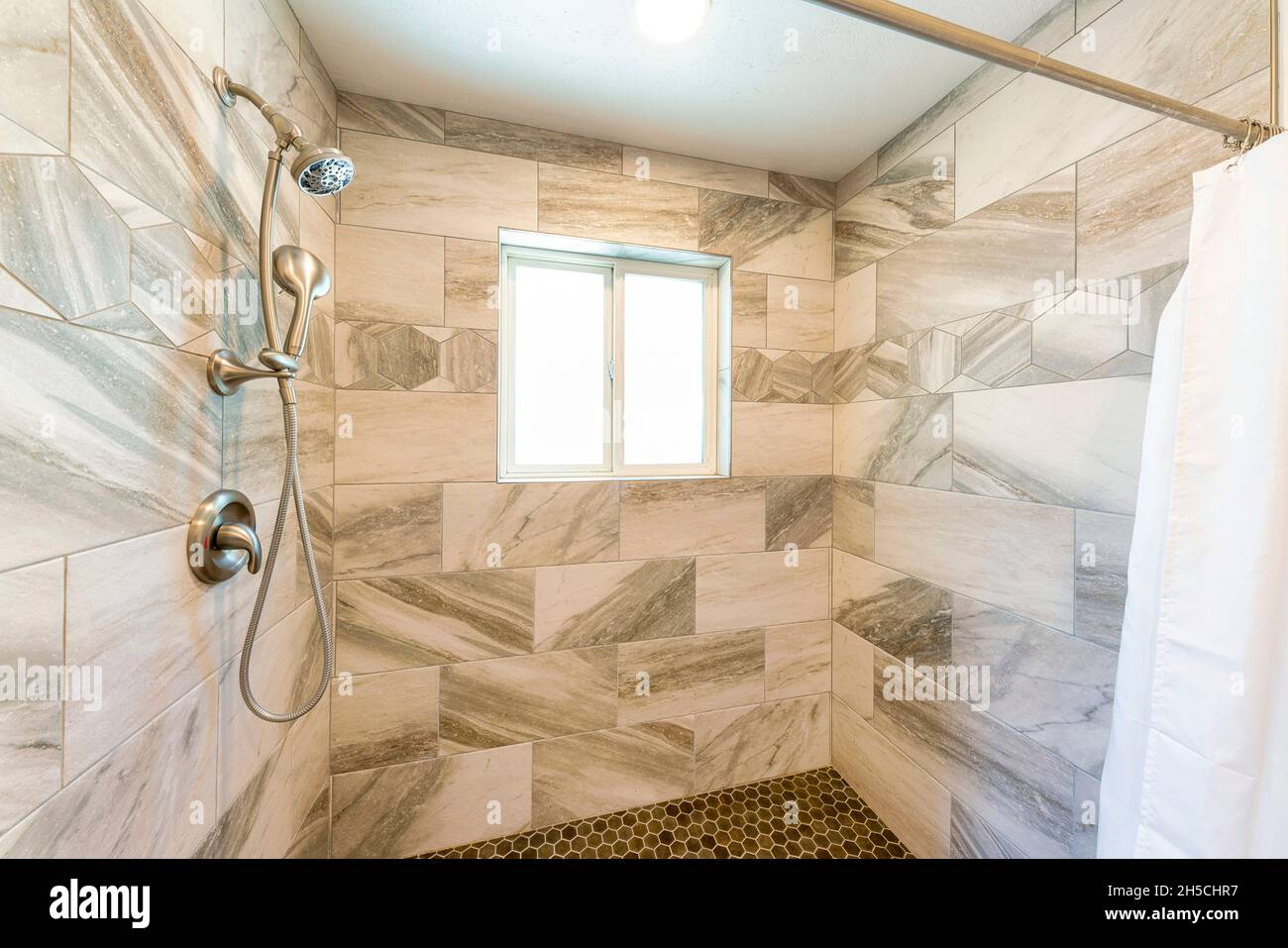 Shower stall interior with marble tile surround and small hexagon pattern tile flooring Stock Photo