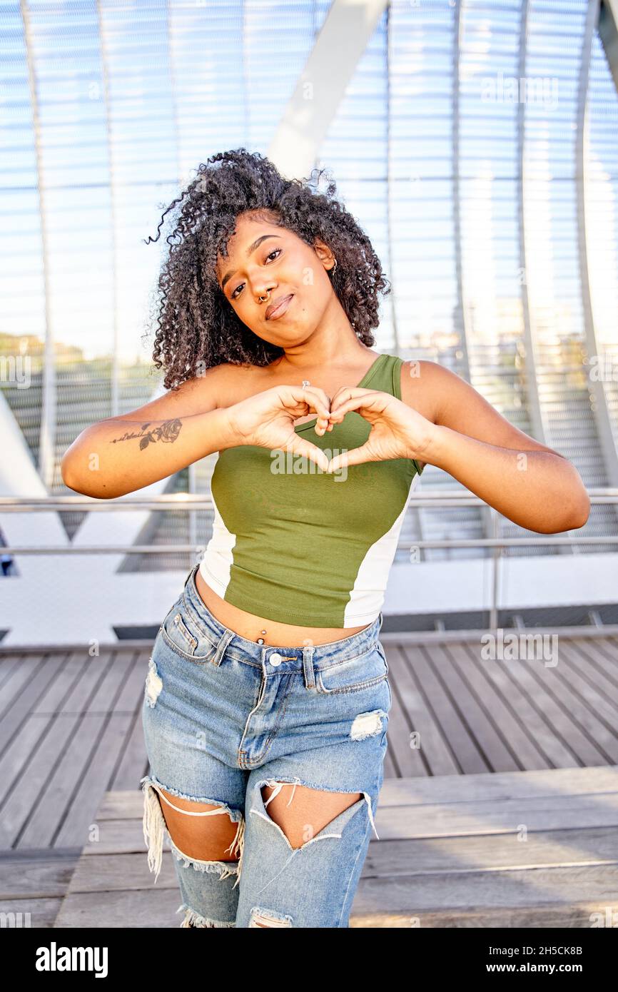 Vertical shot beautiful smiling latin girl showing heart gesture Stock Photo