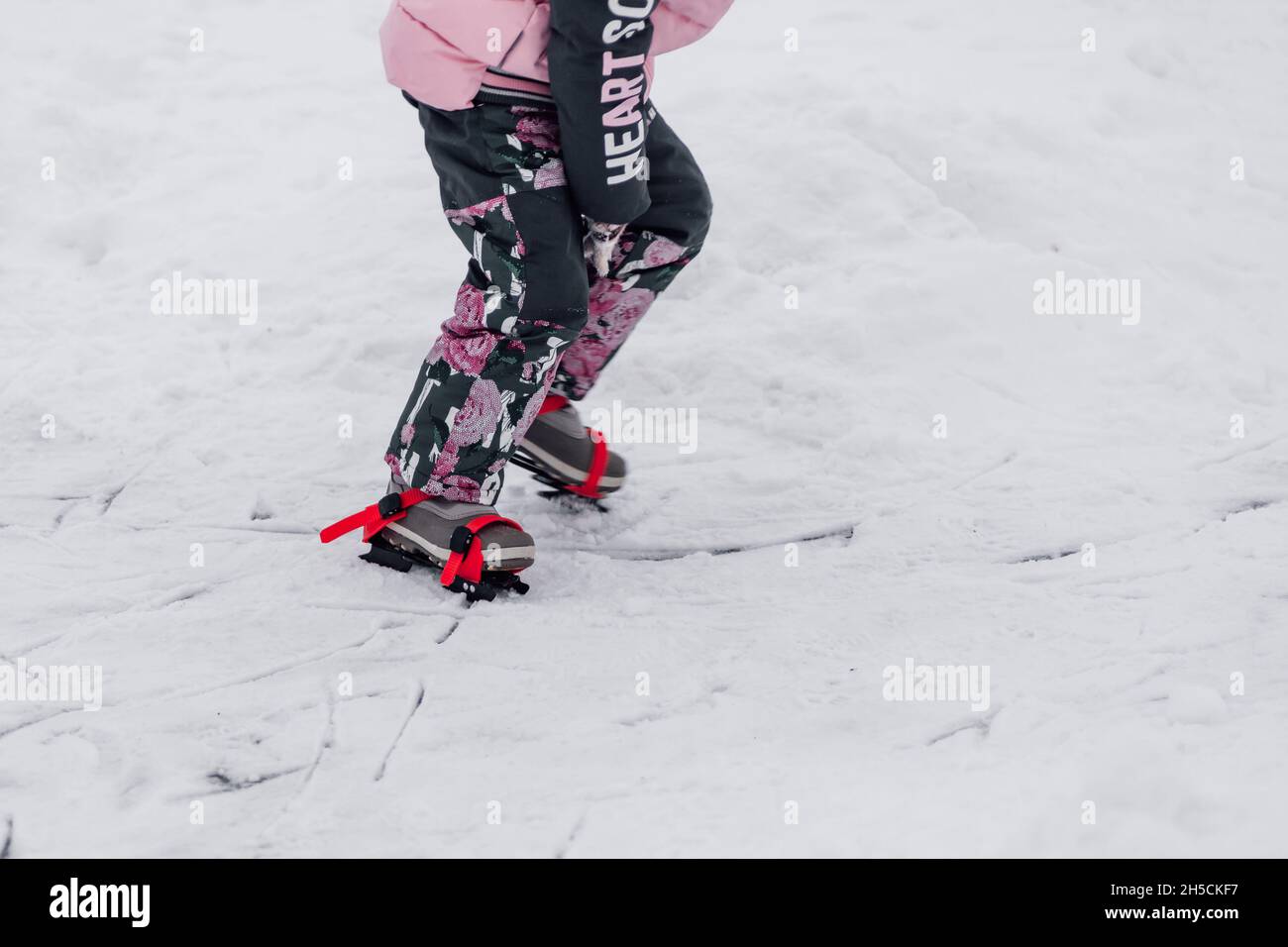 Child learns to skate. Close-up of children figure skates tied to winter boots with red ribbons, side view, snow background Stock Photo