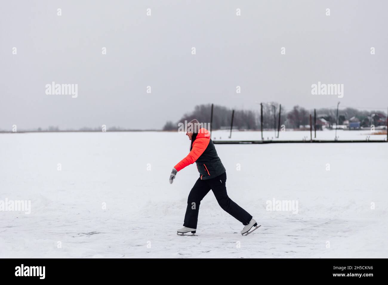 Beautiful woman rides on lake. Young woman in winter clothes enjoys figure skating on frozen ice on frosty day Stock Photo