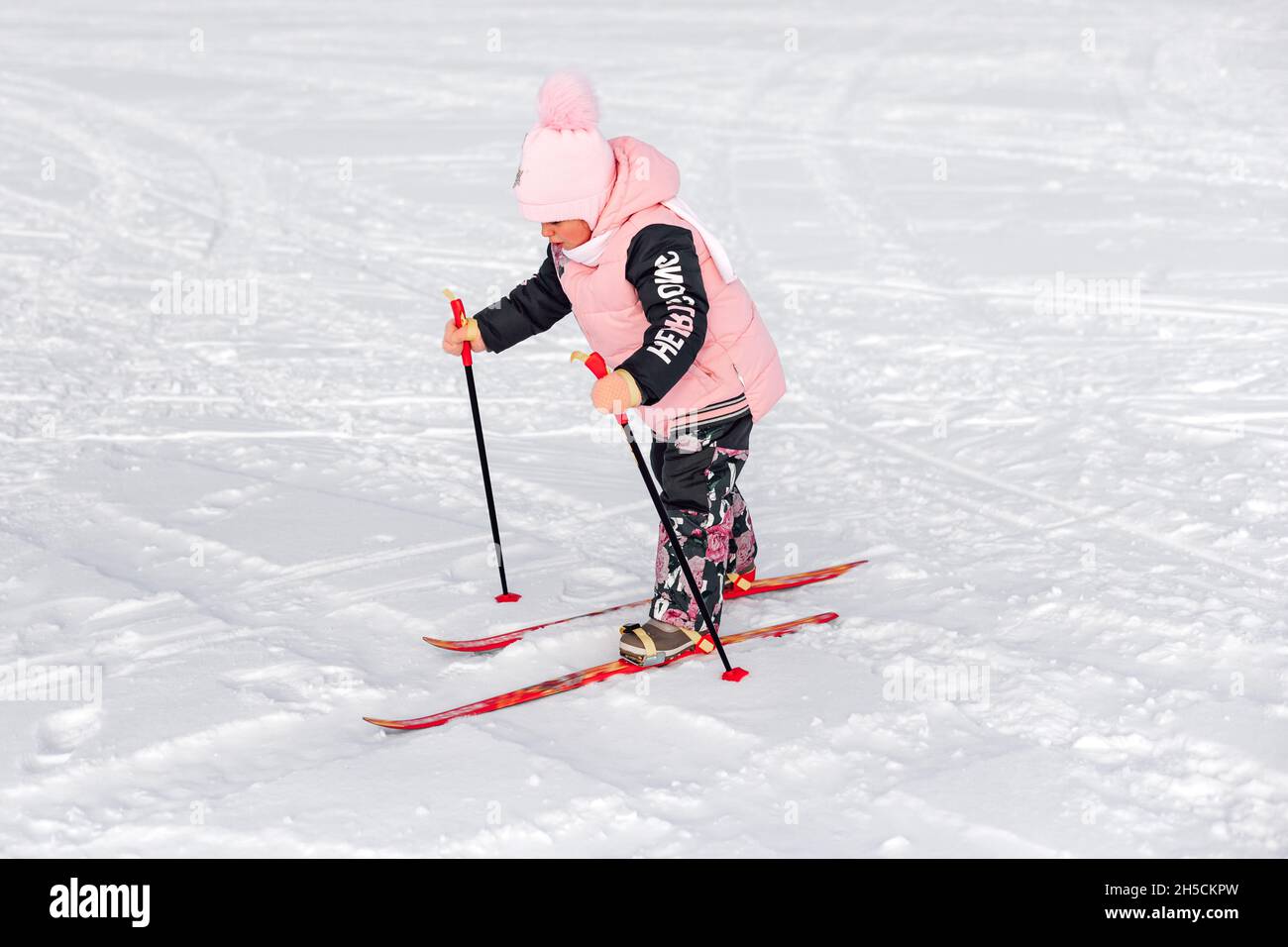 Little girl is skiing. Child in pink warm suit learns to ski on snow-covered road, winter landscape, snow background Stock Photo