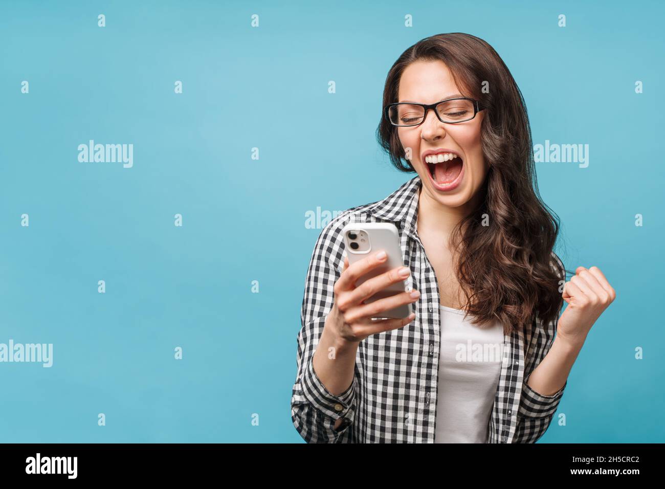 Happy excited female receive a text message informing about salary, rejoices good news, stares at smartphone, gestures actively from happiness Stock Photo