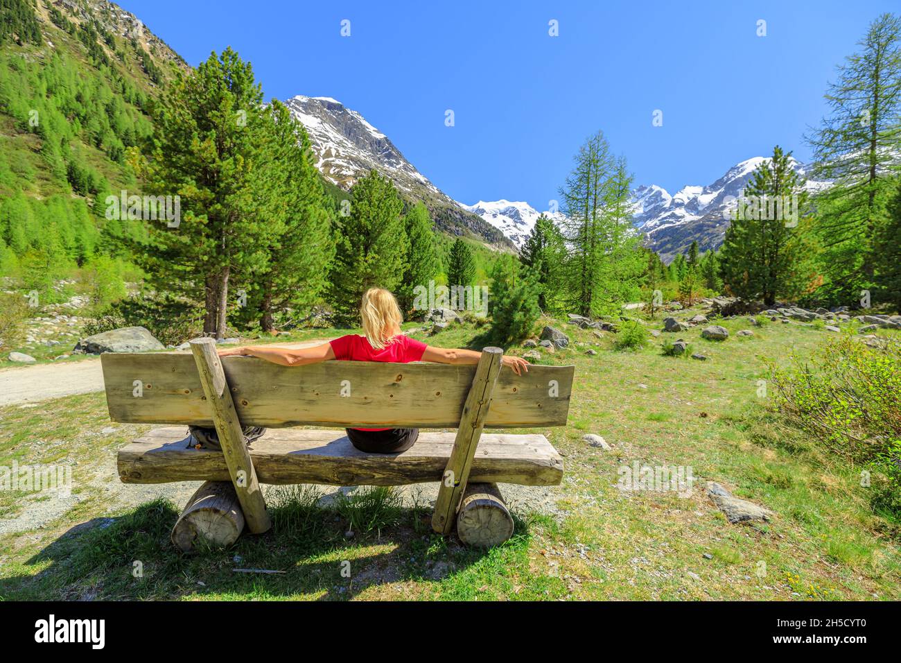 Backpacker girl with red t-shirt on the trekking bench to Morteratsch glacier of Switzerland. Biggest glacier in Bernina Range of the Bundner Alps in Stock Photo