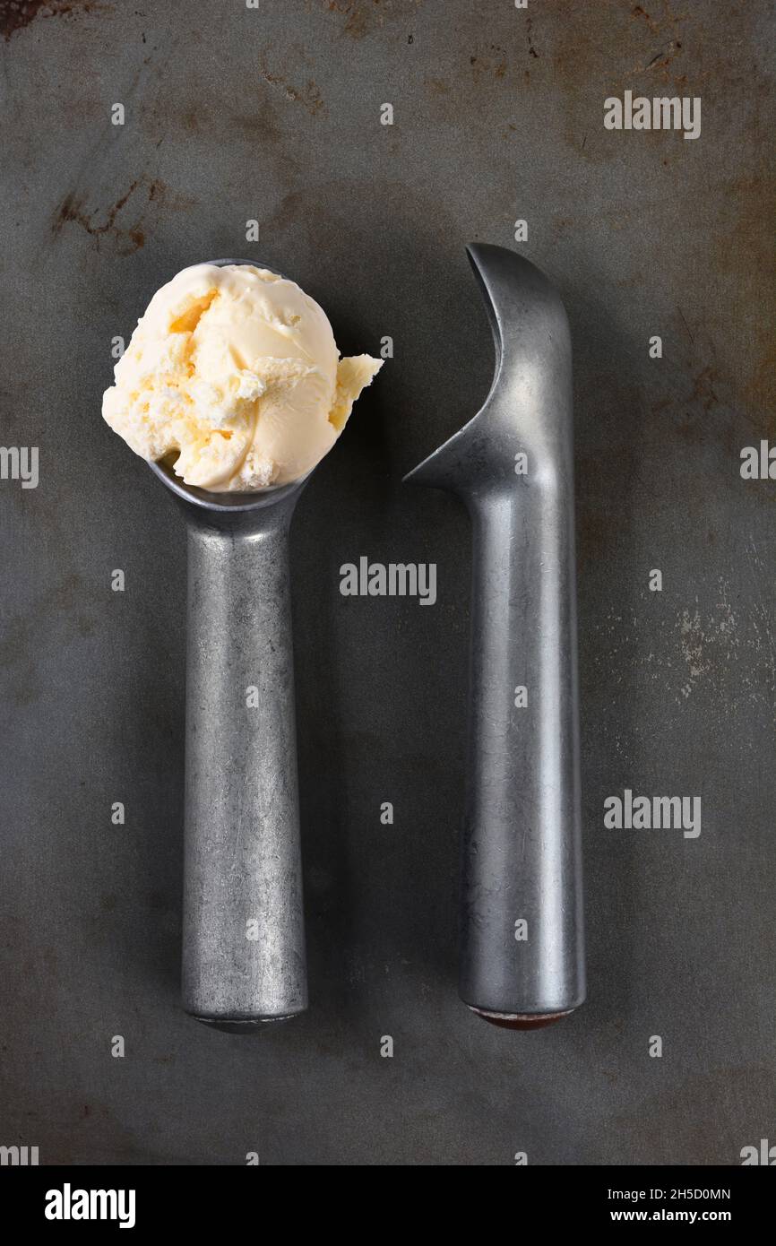 High angle shot of two old fashioned metal ice cream scoops one with a scoop of vanilla. Stock Photo
