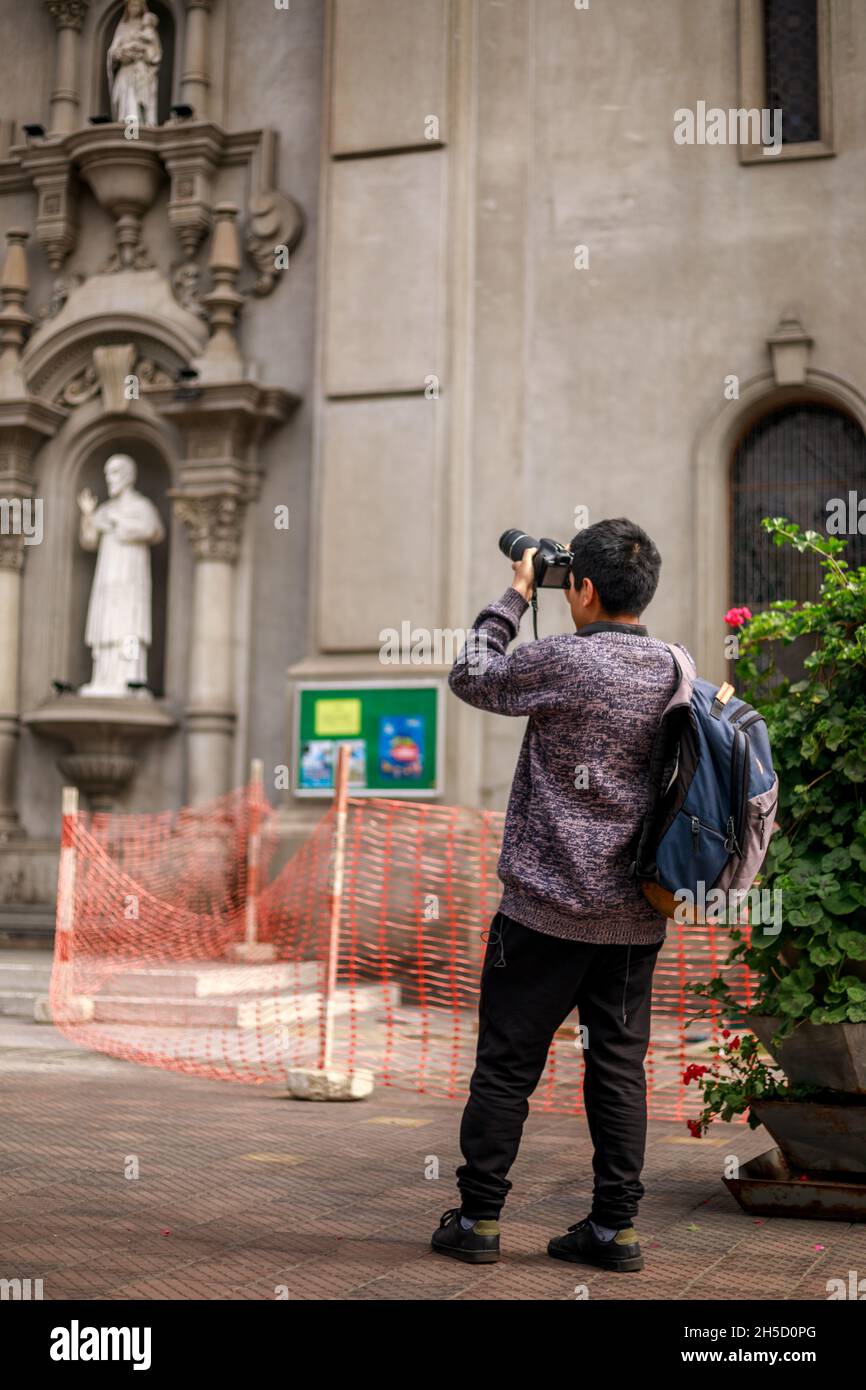 Peruvian teenager wearing a backpack taking a picture with his profesional camera in Lima, Peru Stock Photo