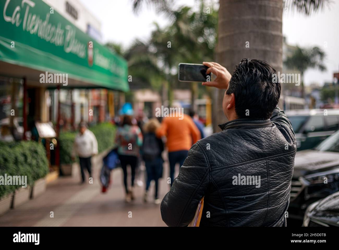 A man taking a picture with his phone on a street in Lima, Peru during daytime. Stock Photo