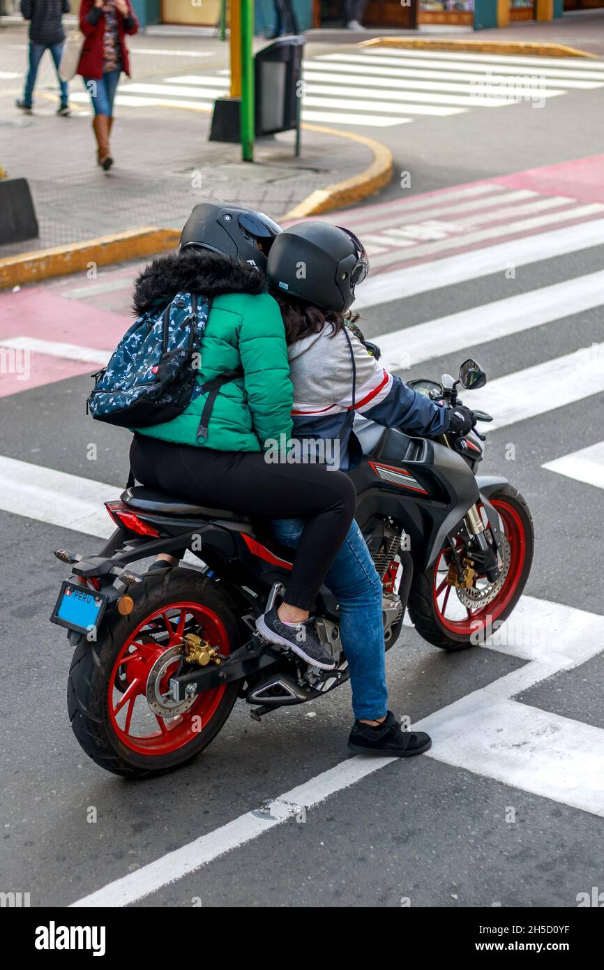 Two women riding a motorcycle and waiting at traffic light on a city street during daytime Stock Photo