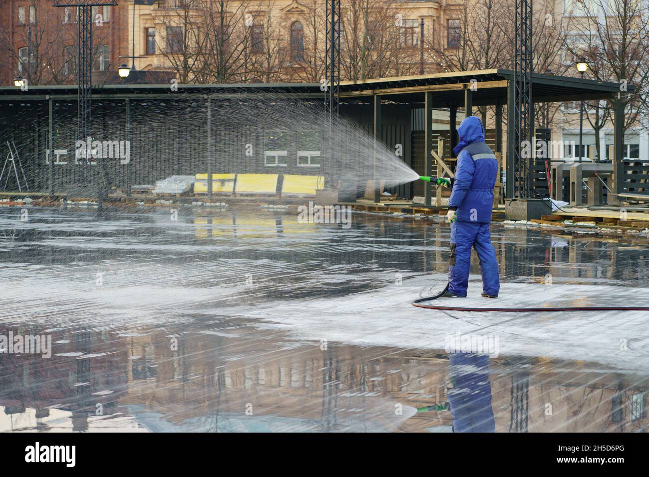 Preparing for winter worker filling area with water for ice rink, outdoor activities in urban