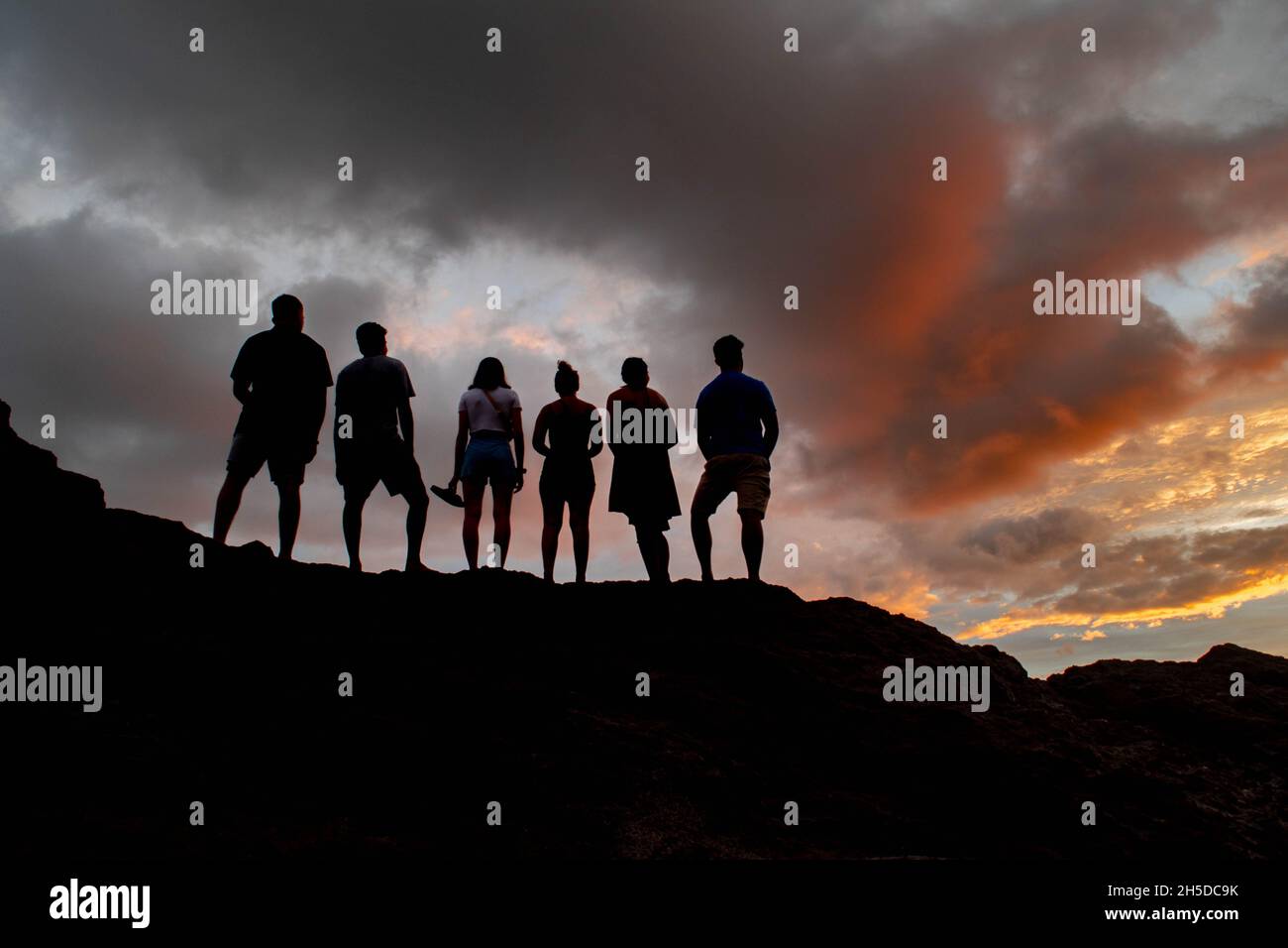 A group of silhouetted friends enjoy the orange sunset in Costa Rica. Stock Photo
