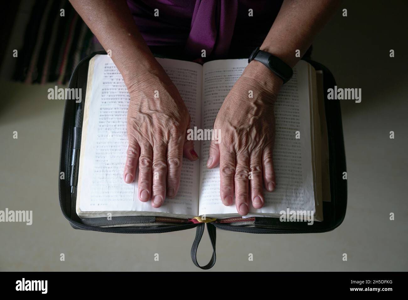 Senior woman wrinkled hands on an open chinese bible. Top view. Stock Photo