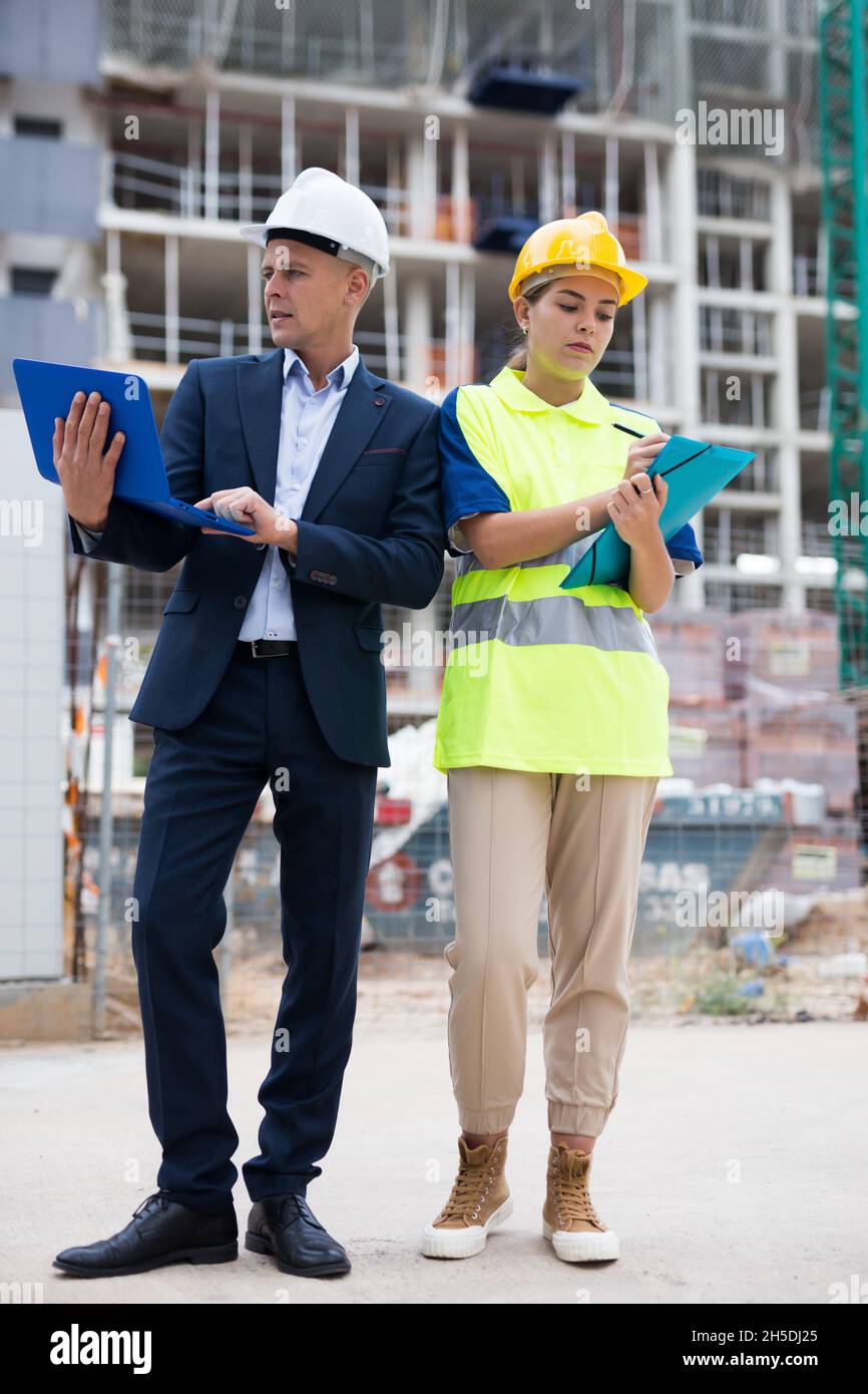 Man engineer standing on a construction site with a young woman worker monitors the construction plan on a laptop Stock Photo