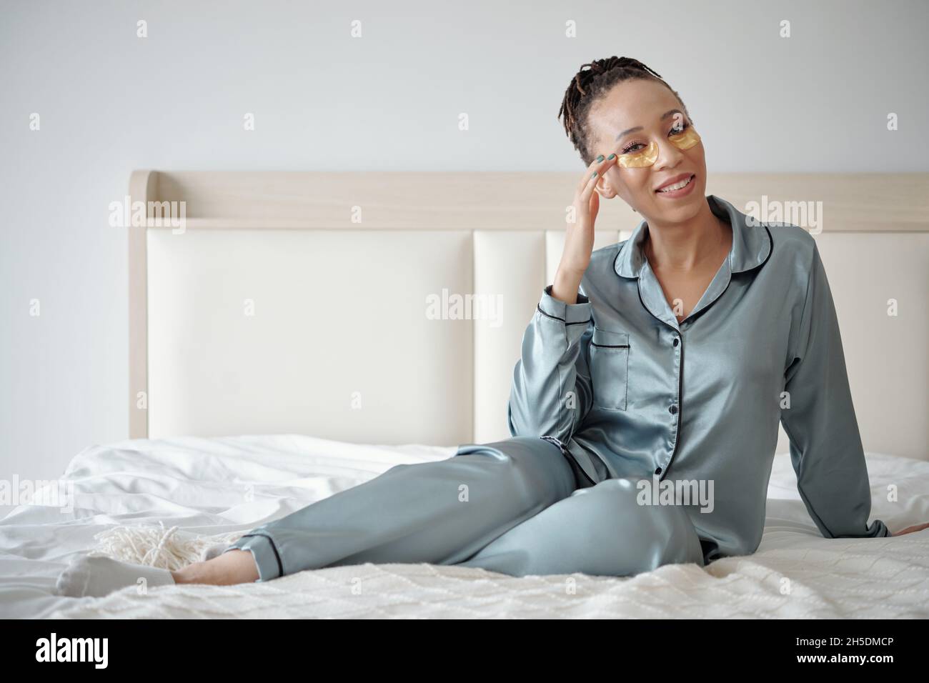 Smiling beautiful Black woman in silk pajamas sitting on comfy bed with moisturizing undereye patches Stock Photo Alamy
