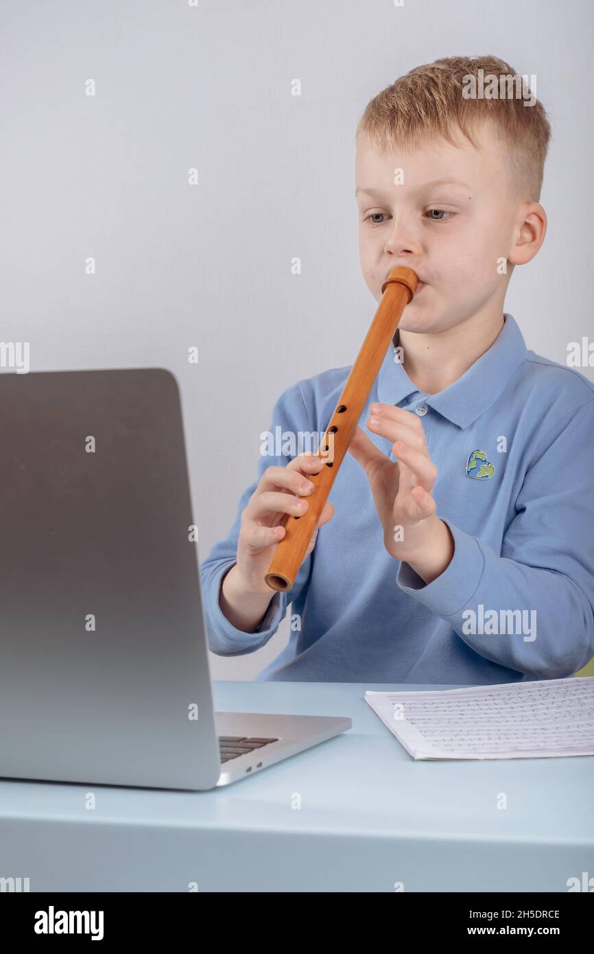 Boy learning to play the flute watching online course on laptop while practicing at home. Online training, online classes. High quality photo Stock Photo