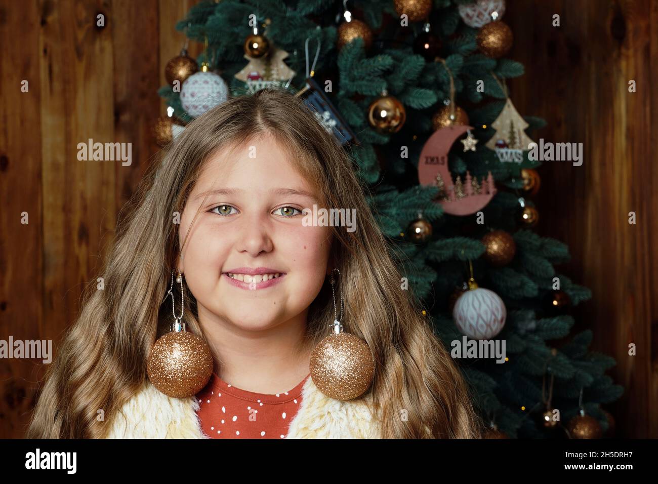 Young happy funny smiling long haired girl on decorated Christmas tree background.. Girl at Xmas. Rustic concept. Humor. Stock Photo