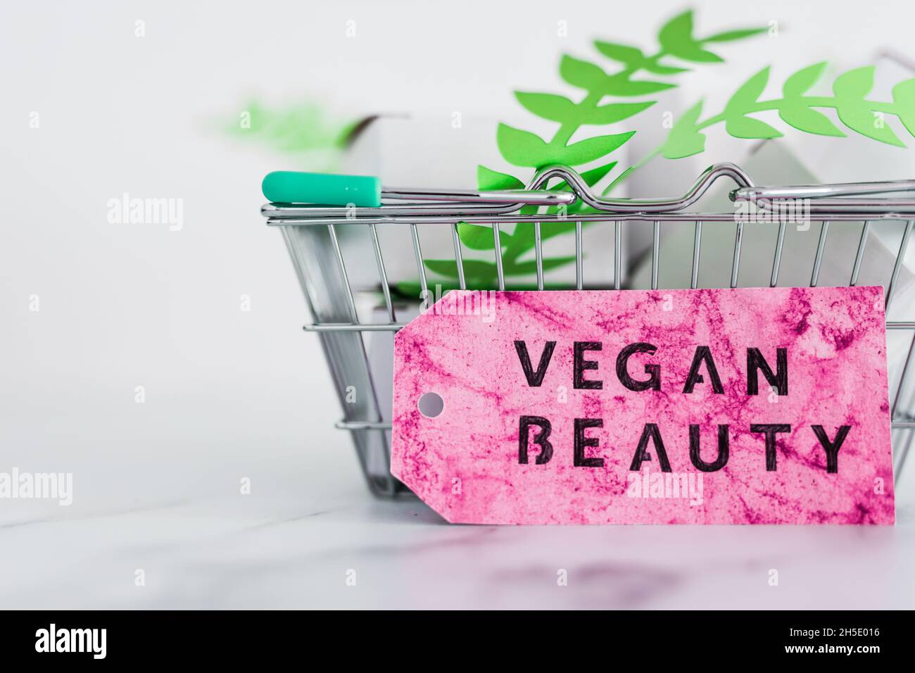 cosmetics and cruelty free product concept, shopping basket with blank product packagings and green leaves with Vegan Beauty label on them Stock Photo