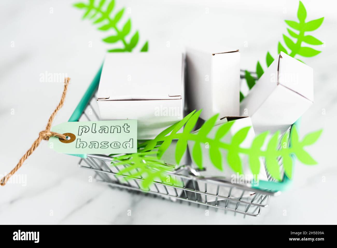 sustainability and cruelty free product concept, shopping basket with blank product packagings and green leaves with Plant-based label on them Stock Photo