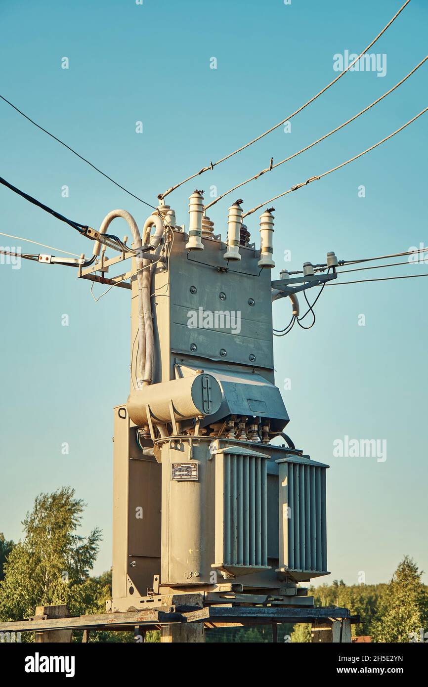 Old grey power transformer with ceramic insulators and connected cables under clear blue sky at sunset light close view Stock Photo