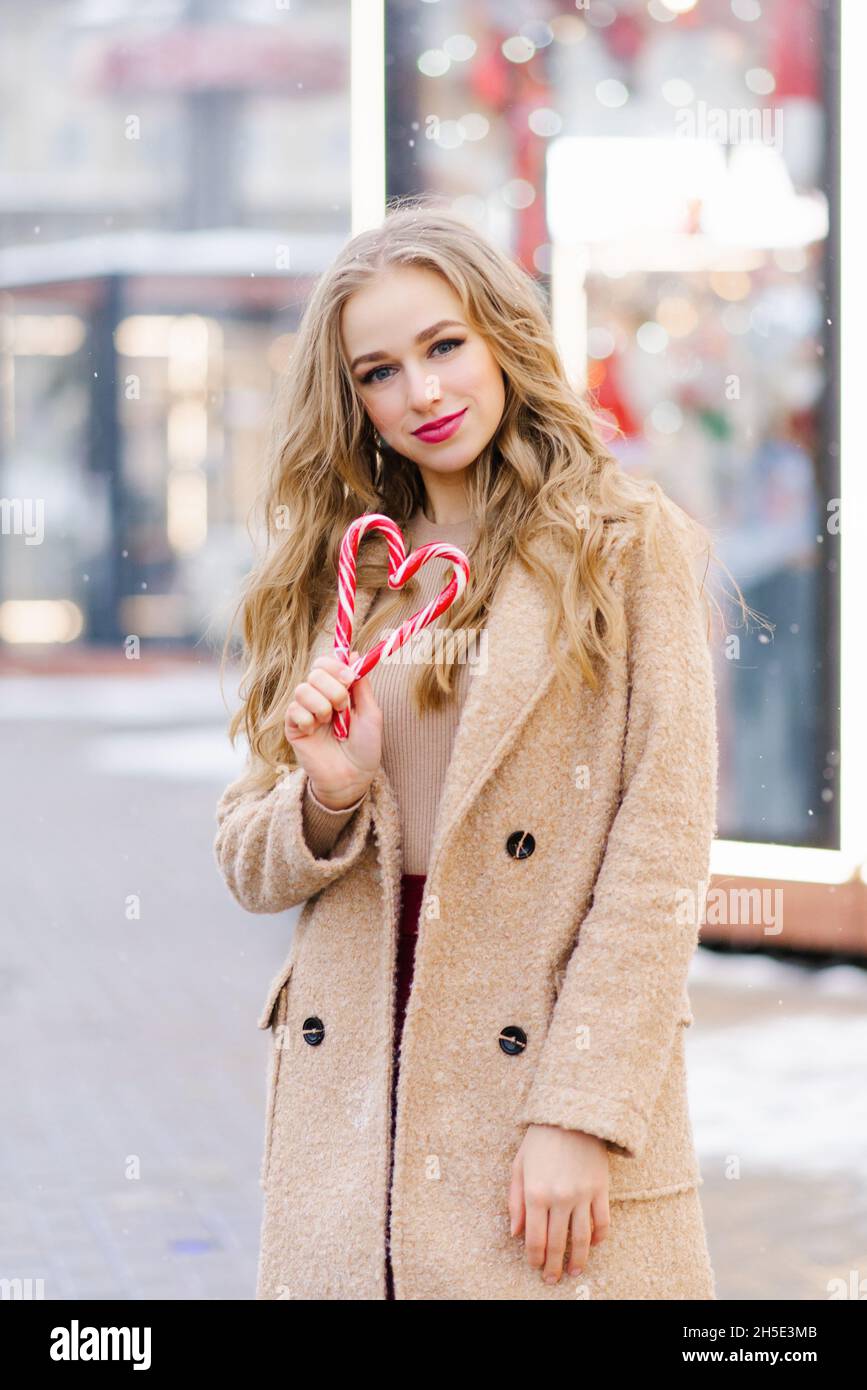 A happy smiling lady poses at a street holiday fair, holding lollipops in her hands. A funny girl makes a heart out of lollipops on a stick. The conce Stock Photo