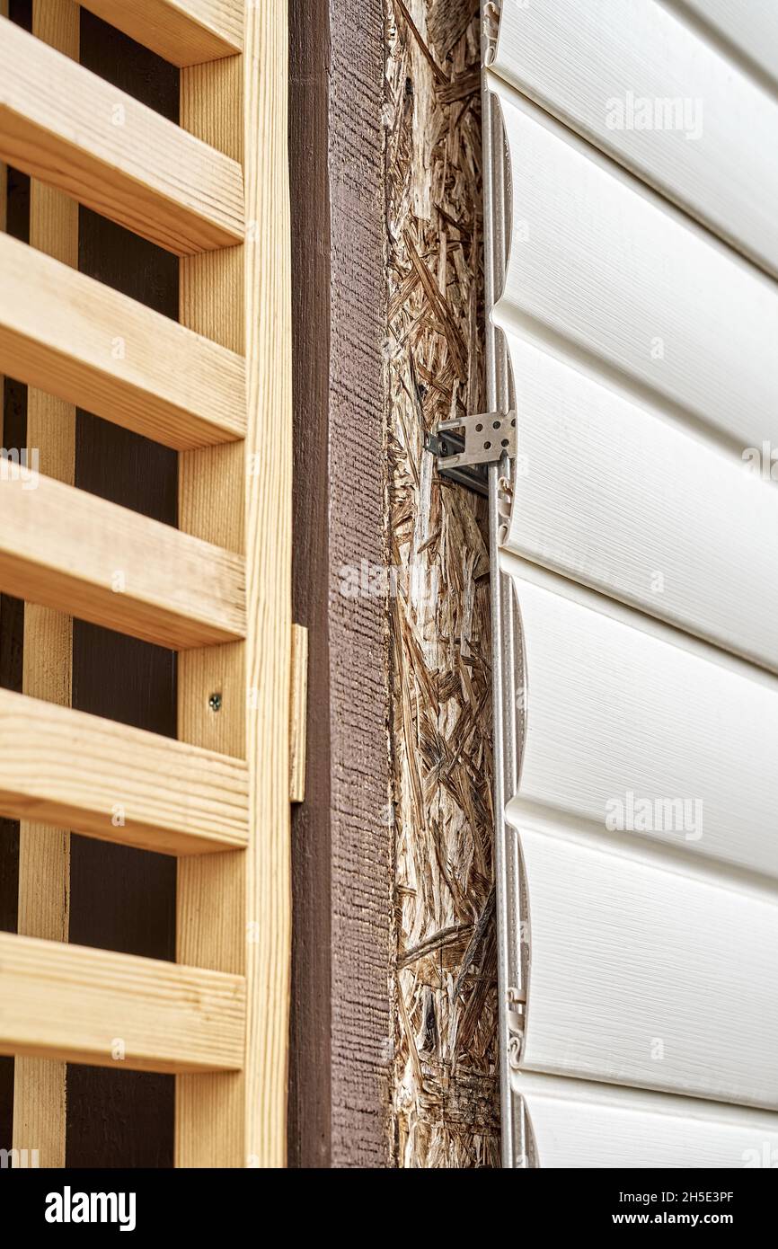 Elegant wooden grid divider near wall of cottage covered with contemporary white plastic siding on spring day close view Stock Photo
