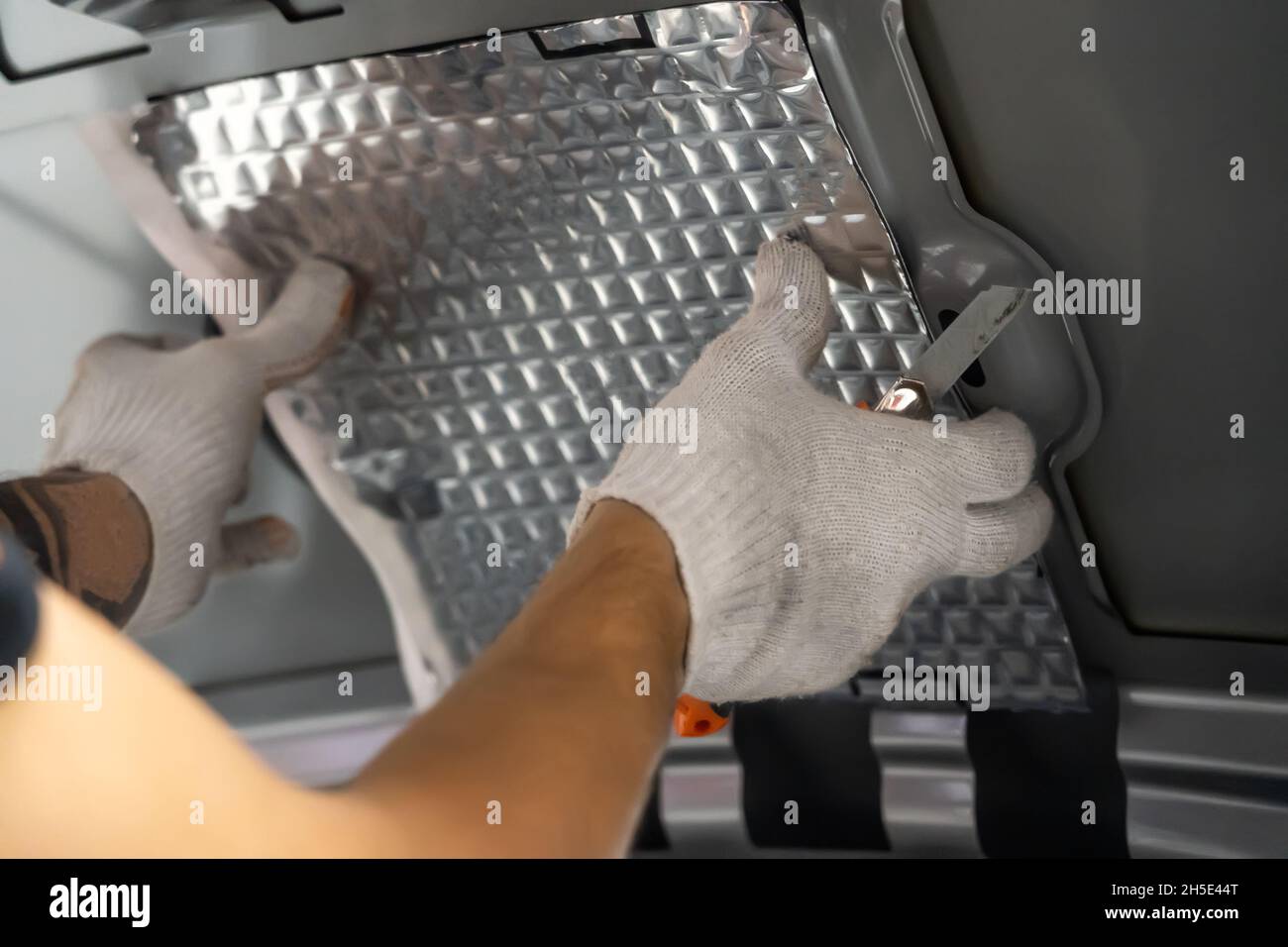 Worker hands glues soundproofing material to inside of car hood