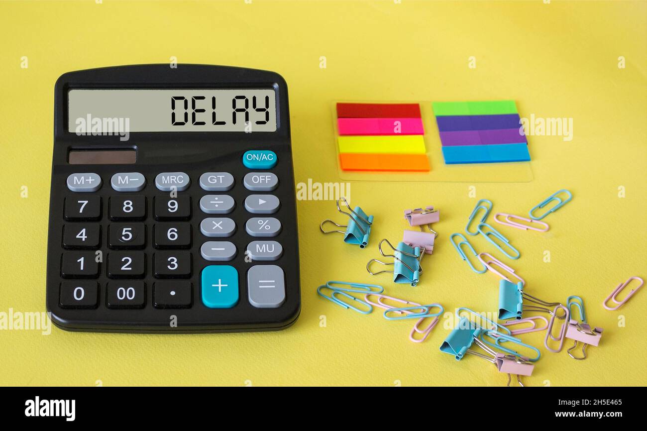 DELAY word on the display of the calculator on a beautiful yellow background with colored stickers and paper clips. Business concept Stock Photo