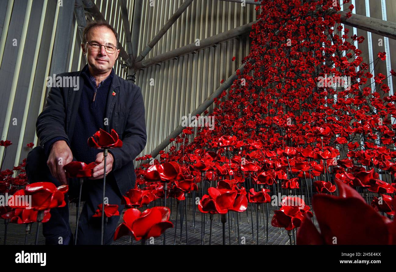 Designer Tom Piper stands beside 'Poppies: Wave and Weeping Window', a new artwork comprising of thousands of handcrafted ceramic poppies cascading 30 metres down and pooling within the Air Shard at IWM North in Manchester. The poppy sculptures were originally part of 'Blood Swept Lands and Seas of Red' at the Tower of London in 2014, and later 'Poppies: Wave and Weeping Window' which toured the UK between 2014 and 2018. Picture date: Tuesday November 9, 2021. Stock Photo