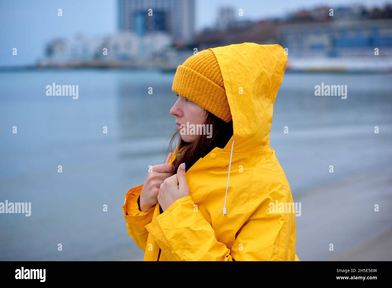 Portrait of pensive woman in yellow coat on the beach in winter Stock Photo