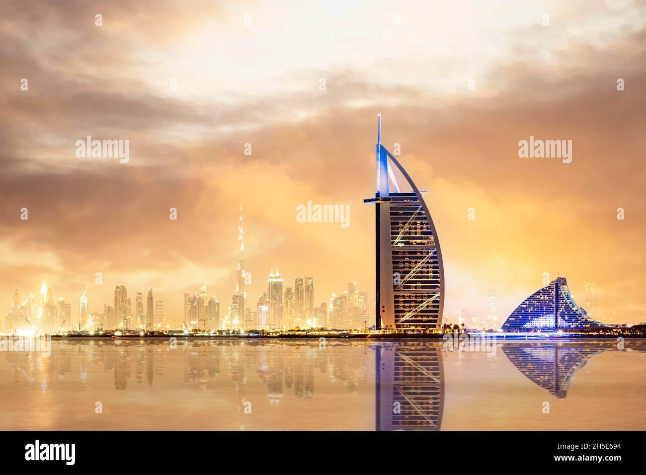 Dramatic sunset over the Dubai skyline with the Burj Khalifa in the distance and the Burj al-Arab luxury hotel in the foreground. Stock Photo