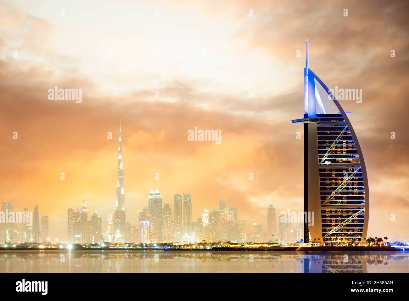 Dramatic sunset over the Dubai skyline with the Burj Khalifa in the distance and the Burj al-Arab luxury hotel in the foreground. Stock Photo