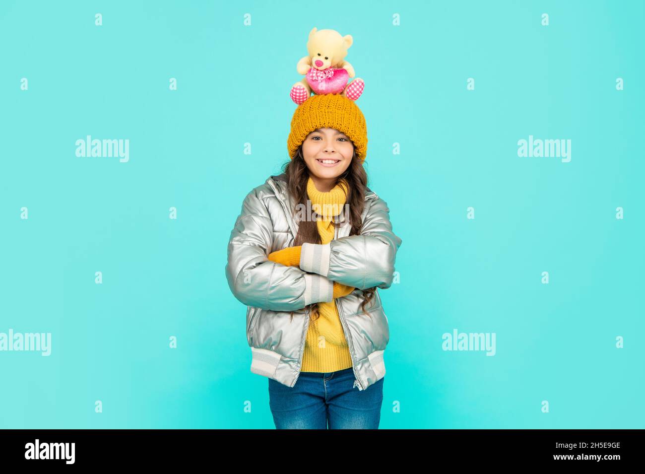 happy teen girl with toy bear crossed hands. child wear warm clothes on blue background. Stock Photo
