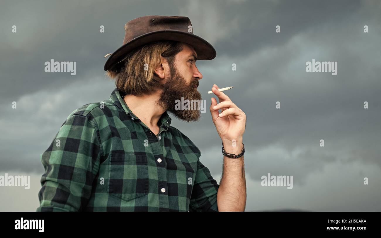 unhealthy way of life. smoking concept. mature brutal hipster in cowboy hat  and checkered shirt. casual fashion style. bearded man holding cigarette  Stock Photo