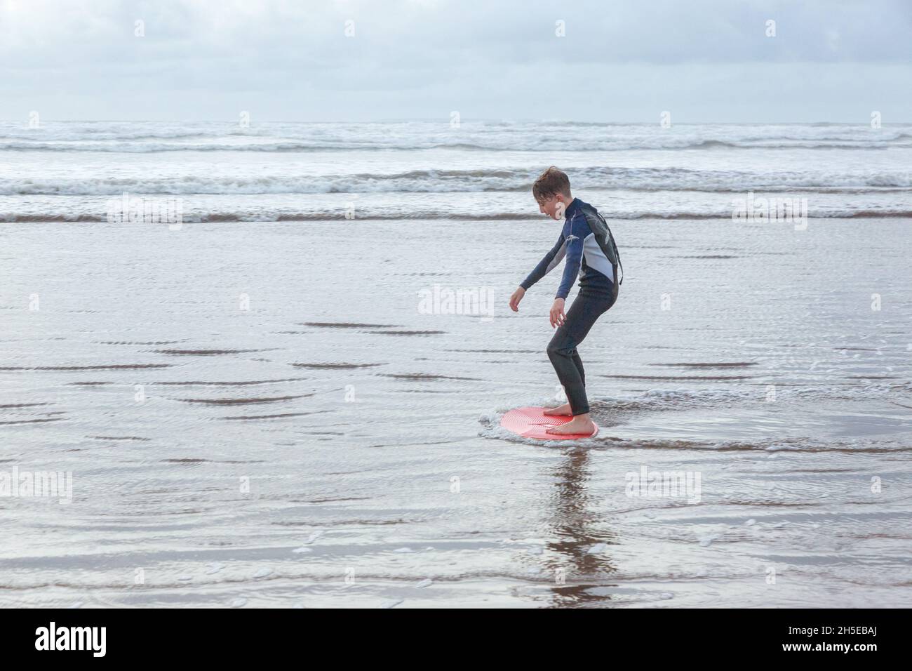 Twelve year old boy skimboarding on Westward Ho! beach,Devon, England, United Kingdom Stock Photo