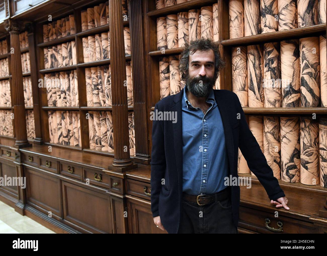 Italian artist Pietro Ruffo poses within his site specific installation 'The Clearest Way' in the Barberini Hall of the Vatican Library transformed âinto a lush tropical forestâ with Ruffo's rolled botanical prints lining the 17th-century wooden bookcases on November 08, 2021at the Vatican. The Apostolic Library is opening up to the public for the first time with a dedicated space for temporary exhibitions of contemporary art by Italian artist Pietro Ruffo. The exhibit goes under the title âEveryone: Humanity on its way, recalls the Pope s encyclical Fratelli tutti, and turns part of the Stock Photo