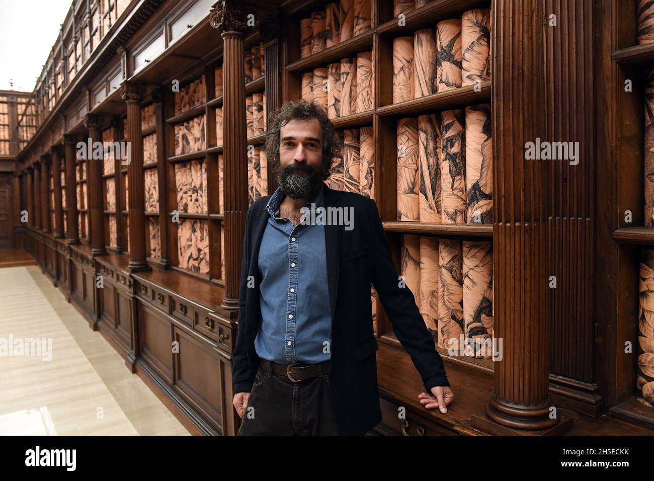 Italian artist Pietro Ruffo poses within his site specific installation 'The Clearest Way' in the Barberini Hall of the Vatican Library transformed âinto a lush tropical forestâ with Ruffo's rolled botanical prints lining the 17th-century wooden bookcases on November 08, 2021at the Vatican. The Apostolic Library is opening up to the public for the first time with a dedicated space for temporary exhibitions of contemporary art by Italian artist Pietro Ruffo. The exhibit goes under the title âEveryone: Humanity on its way, recalls the Pope s encyclical Fratelli tutti, and turns part of the Stock Photo