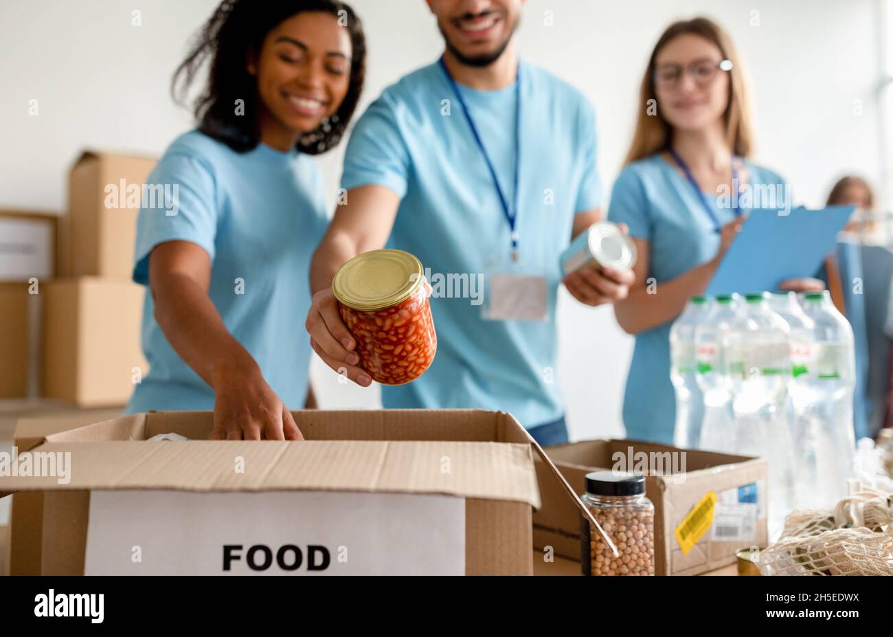 Millennial volunteers putting jars in box while sorting donated food, working in community charity donation center Stock Photo