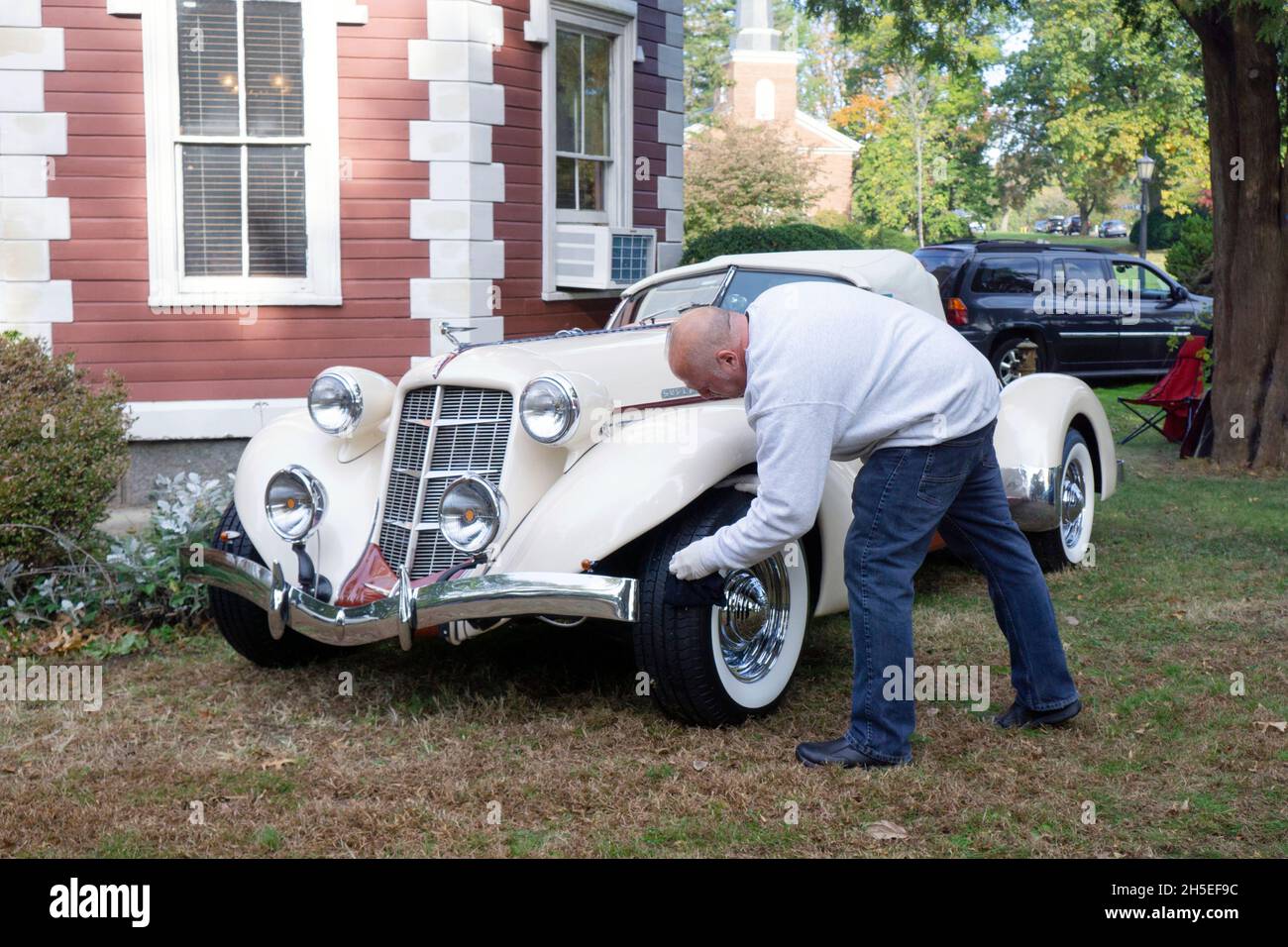 The owner of an antique 1936 Auburn Boattail Speedster convertible cleans his tires. At a vintage car show.in Bayside, Queens, New York Stock Photo