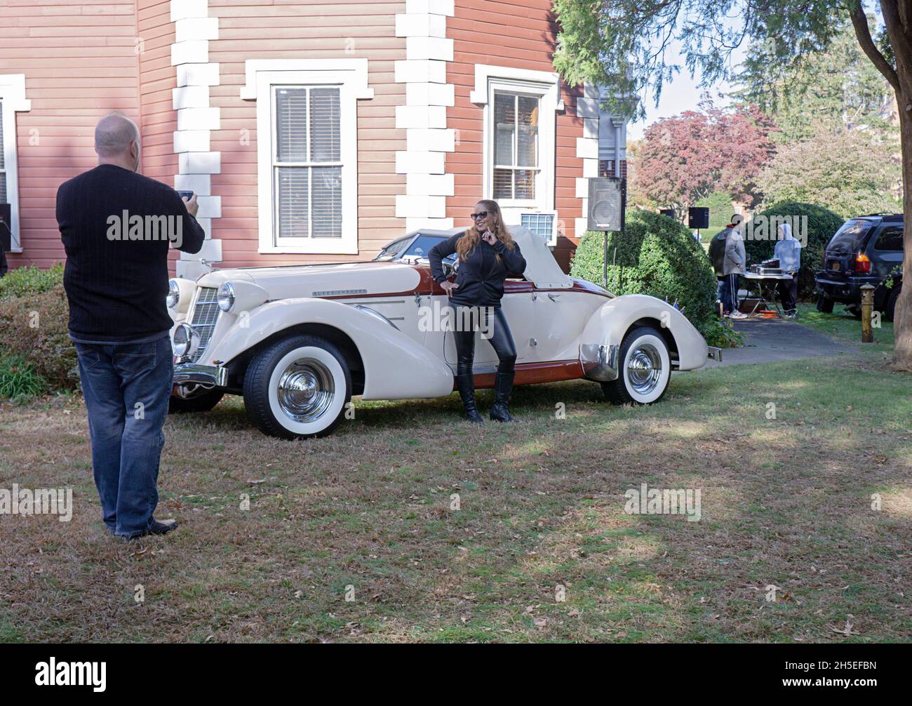 The owner of a1936 Auburn Boattail Speedster photographs his significant other. At a vintage car show at the Bayside Historical Society, Queens, NYC. Stock Photo