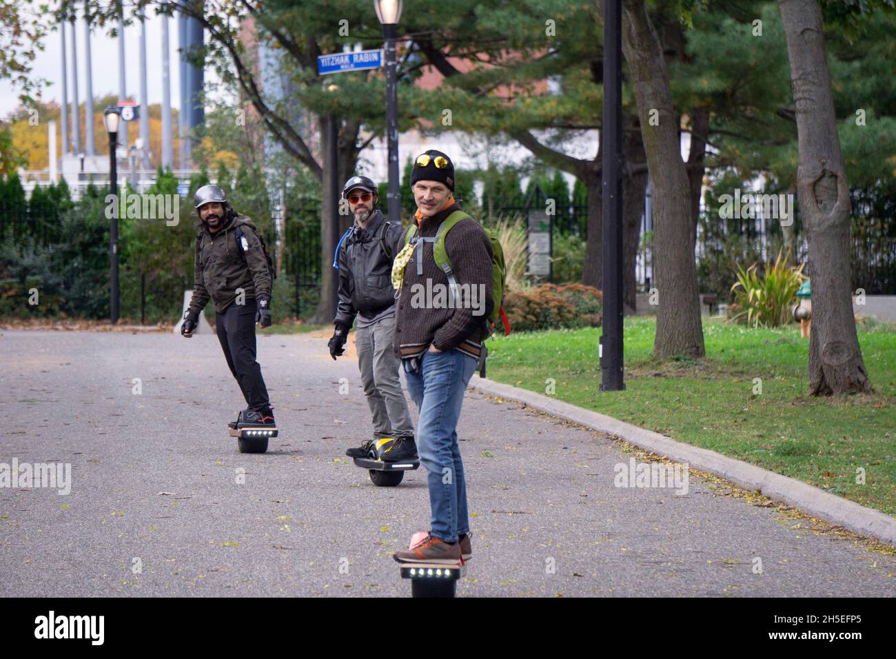 3 men, each riding a ONEWHEEL, a self-balancing single wheel electric board-sport, described as an electric skateboard. In Queens, New York City. Stock Photo