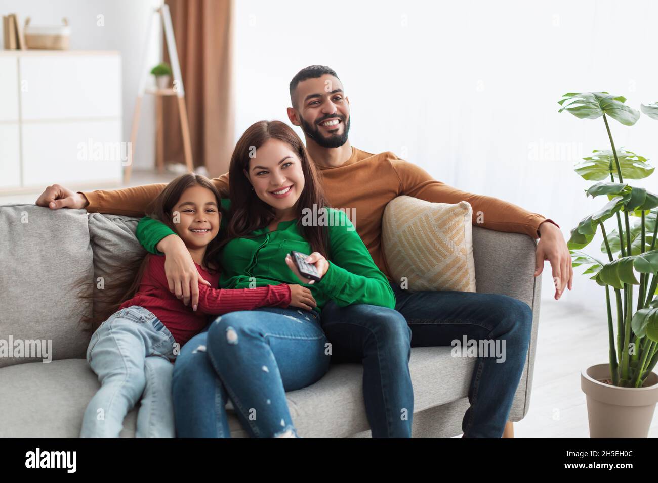 Happy young Arab family watching television sitting on sofa Stock Photo