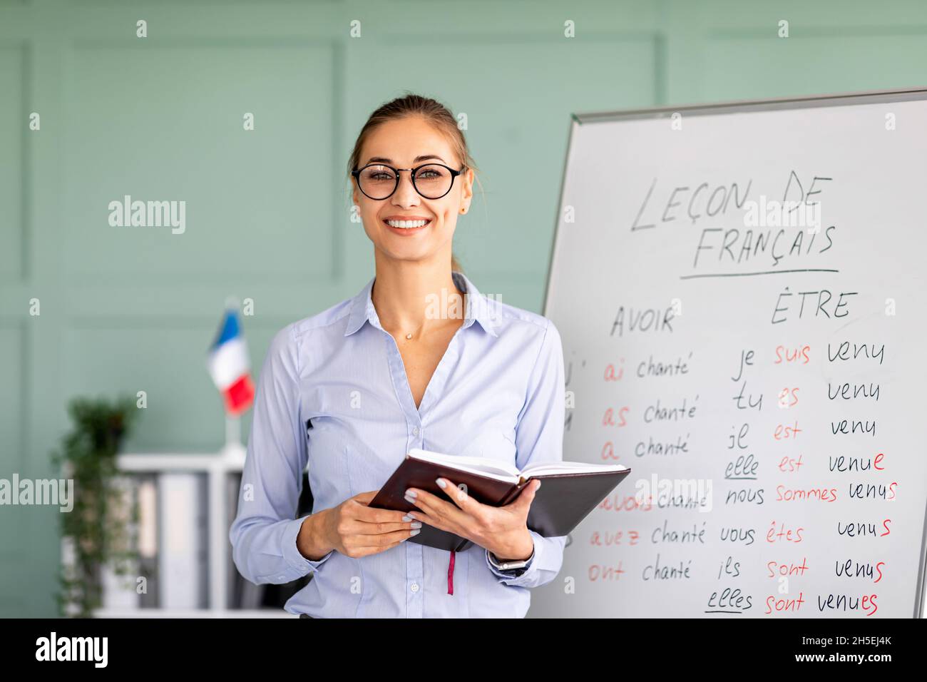 Learning and knowledge concept. Young smiling woman posing near whiteboard with French language grammar rules Stock Photo