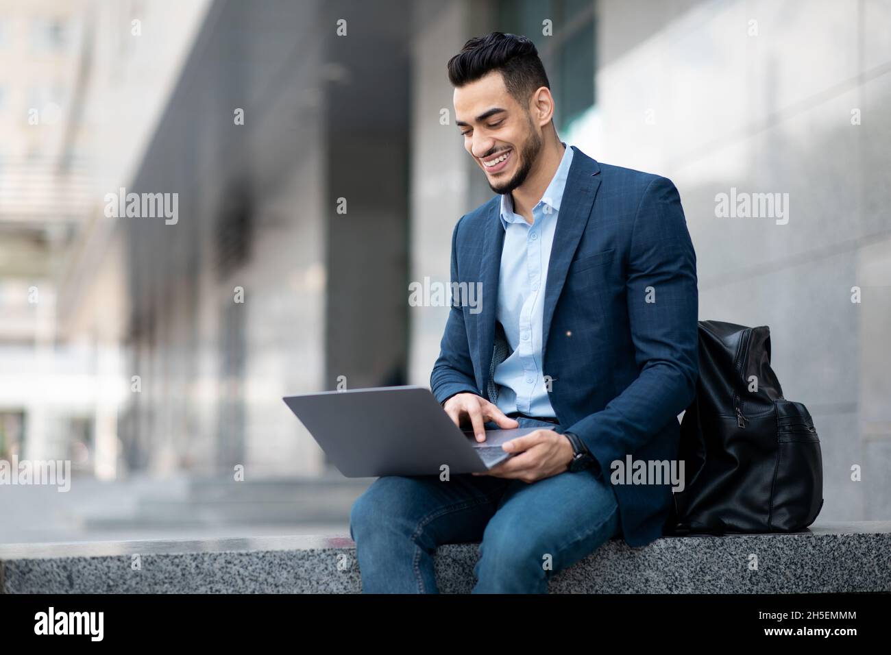 Positive middle eastern guy sitting on the street, using laptop Stock Photo