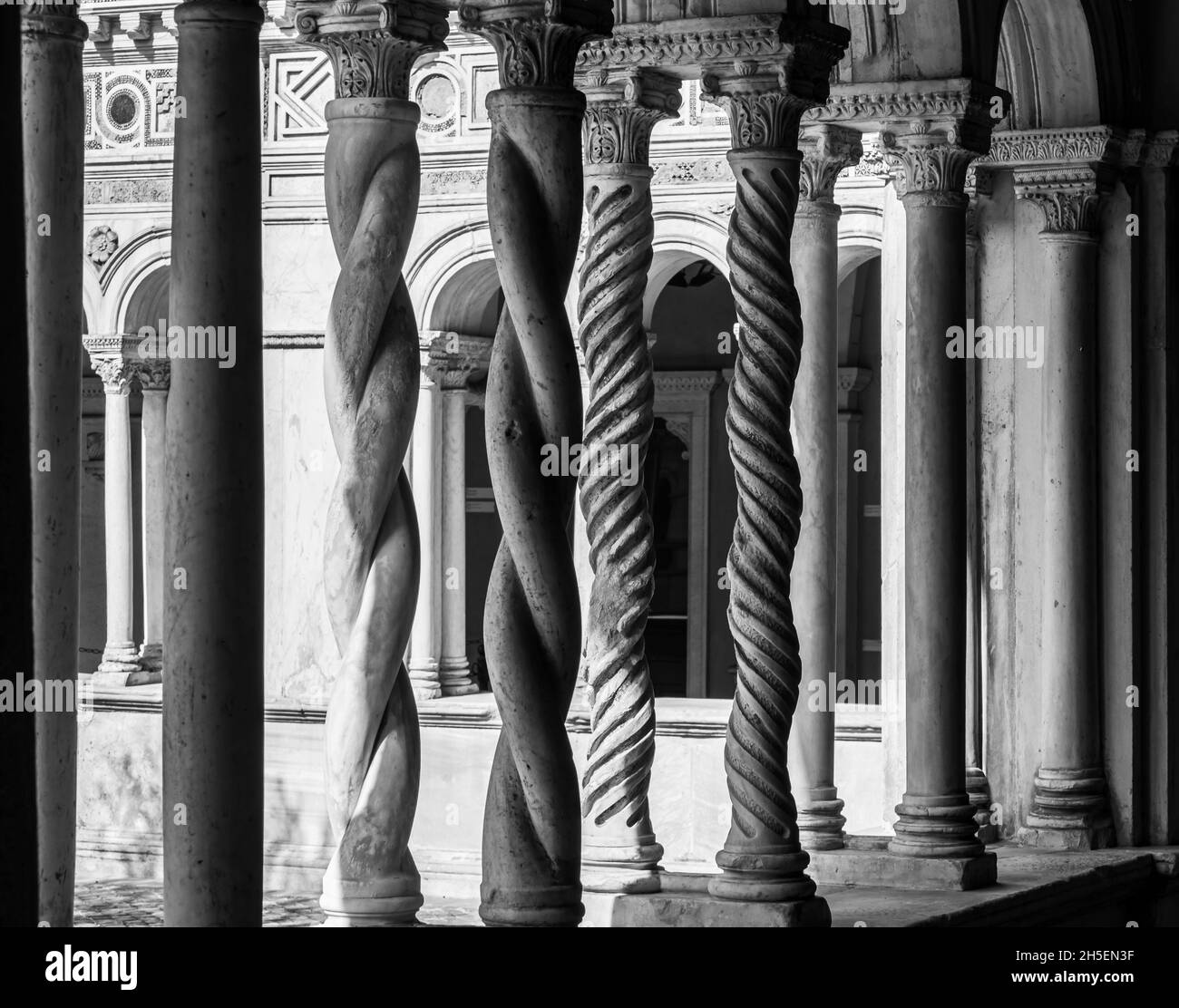 Black and white photo of curved decorated pillars sustaining arches in the interior patio of a medieval monastery in Italy Stock Photo