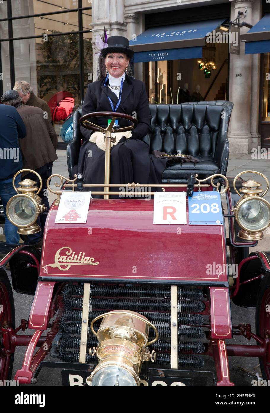 A smiling lady in period costume, sits aboard a Maroon, 1904, Cadillac, during the Regents Street Motor Show Concours d'Elegance, November 2021 Stock Photo