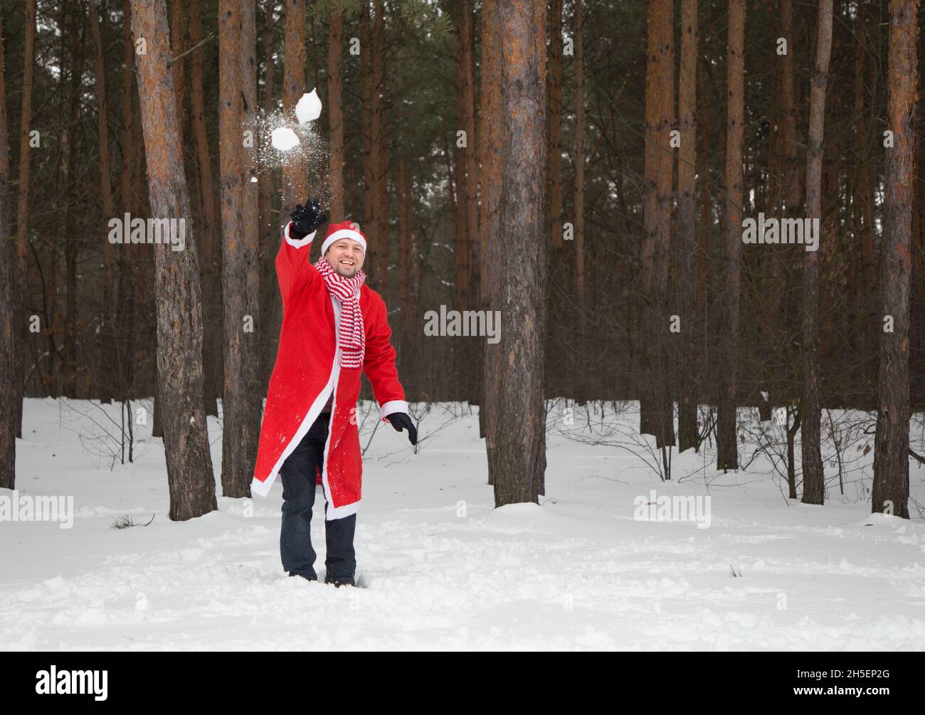 cheerful man in a Santa suit throws snowballs in a snowy forest. Christmas Eve, merry snowy winter. Waiting for a miracle, winter joys Stock Photo