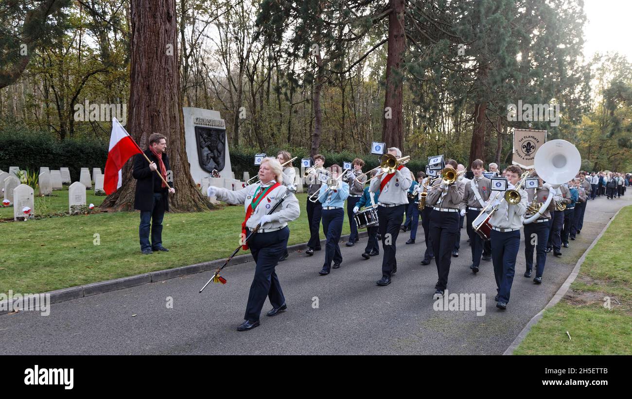 Sunday 7th November 2021. Brookwood Last Post Association hold their monthly service with hundreds of scouts, guides & the 1st Claygate Scout & Guide Band. Here the band process past the Czechoslovakian National Monument (in background)  and a man holding the Polish National flag. Air Forces Shelter, Brookwood Military Cemetery, Surrey. Stock Photo