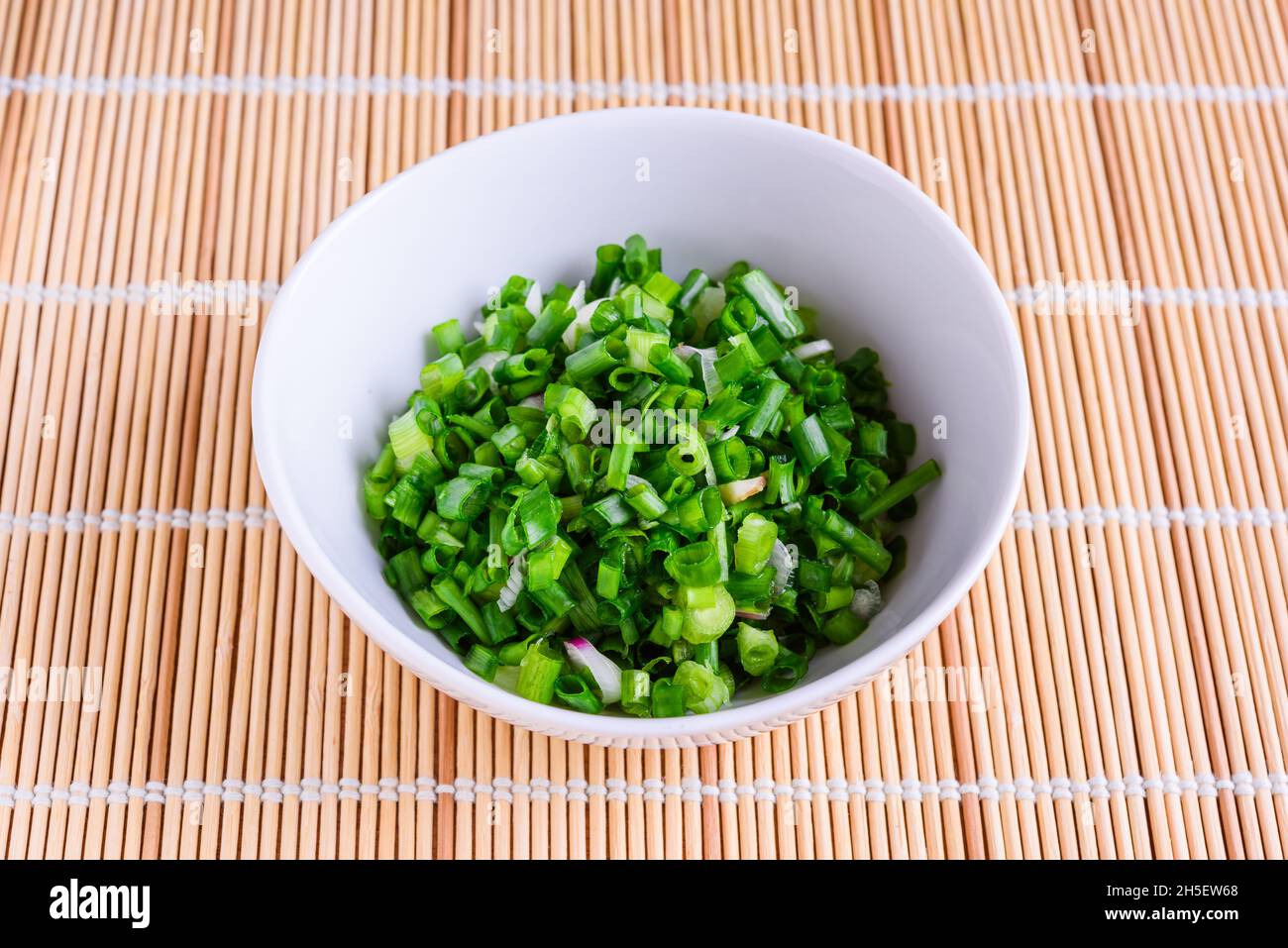 Freshly cut spring onions in white bowl as cooking ingrdients. Stock Photo