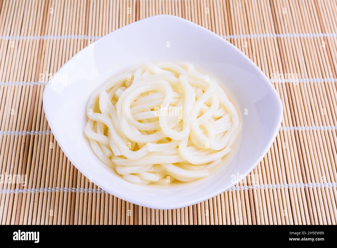 Freshly prepared Japanese udon noodles in white bowl on bamboo mat Stock Photo