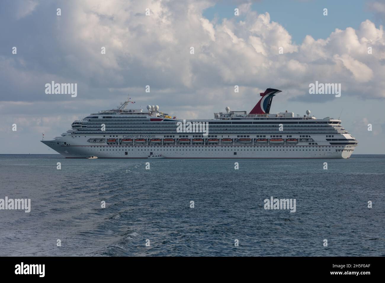 Belize coast - January 1, 2020: Aerial shot of Carnival Freedom anchored off the coast of Belize and two small tender boats by her side. Blue sky and Stock Photo