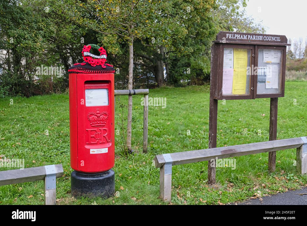 Felpham Village Post Box yarn bombed with crocheted Poppy Wreath bearing the lettering 'Lest We Forget' Stock Photo