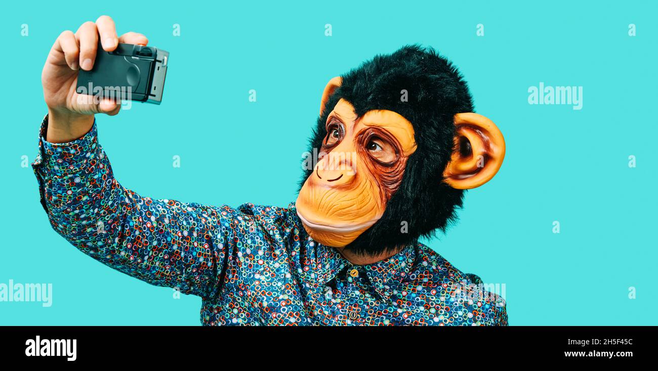 closeup of a man, wearing a monkey mask, taking a selfie with a retro film camera, on a blue background, in a panoramic format to use as web banner or Stock Photo